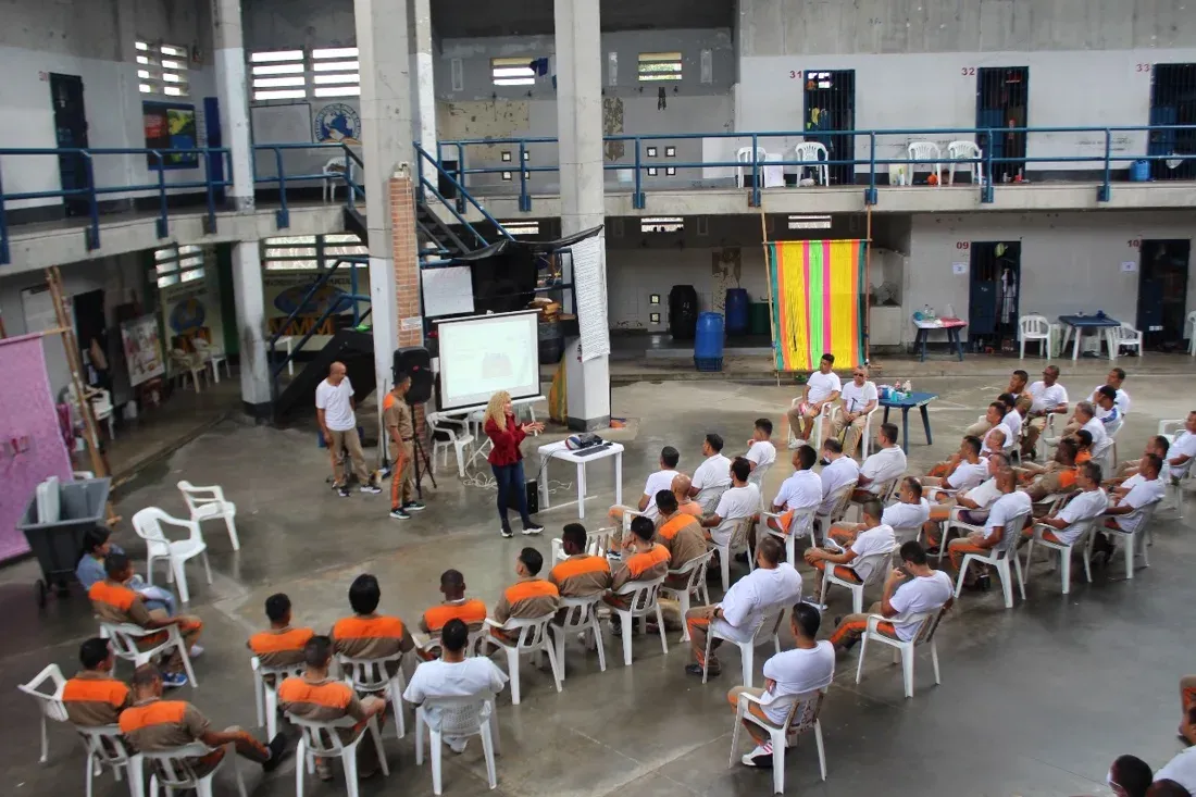 Leslye Rendón comparte una conferencia ante un grupo de personas sentadas en el patio de un centro penitenciario.